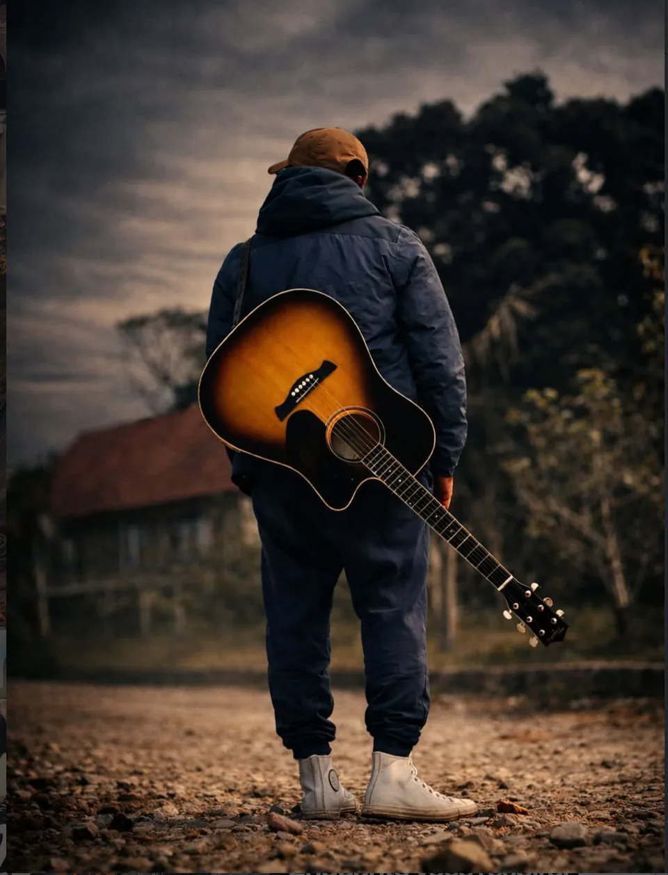 Lukas Cruz de costas, com violão, em estrada de terra